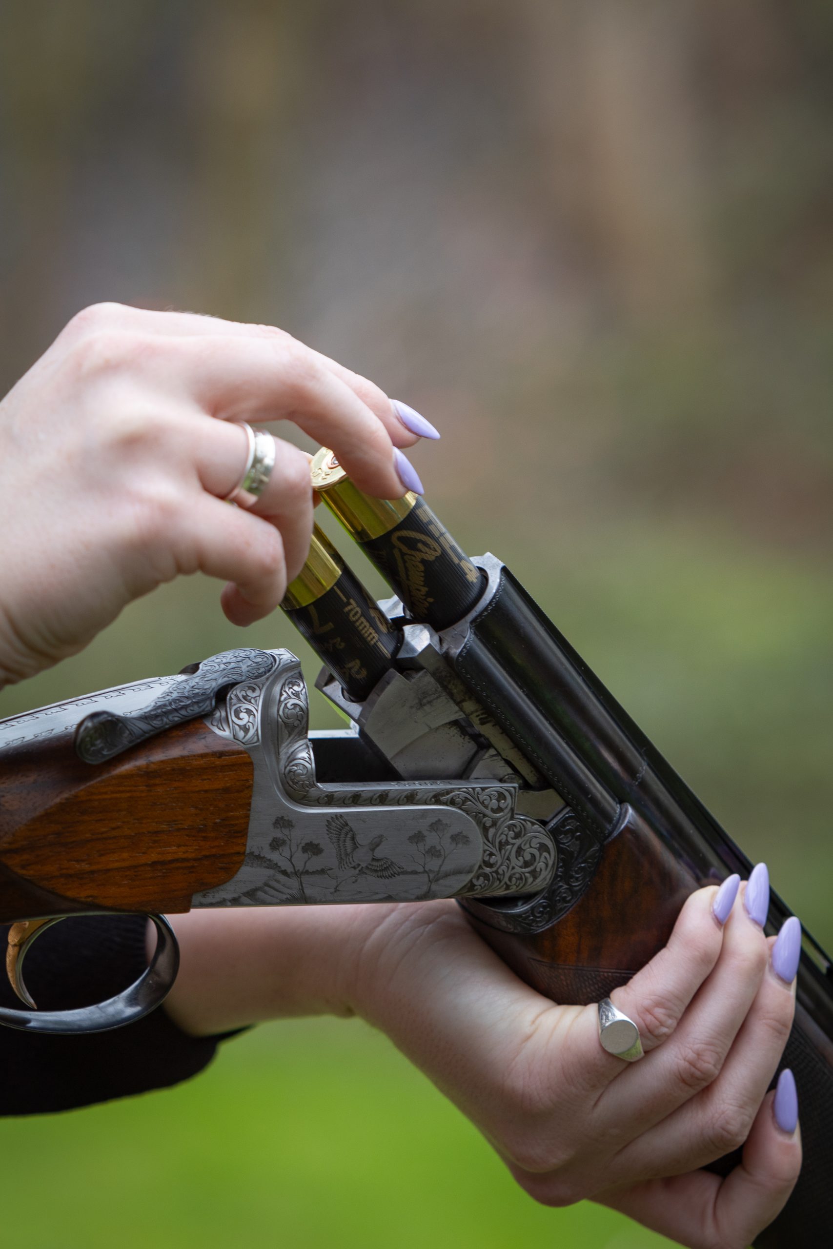 A woman sliding two cartridges into her over and under shotgun