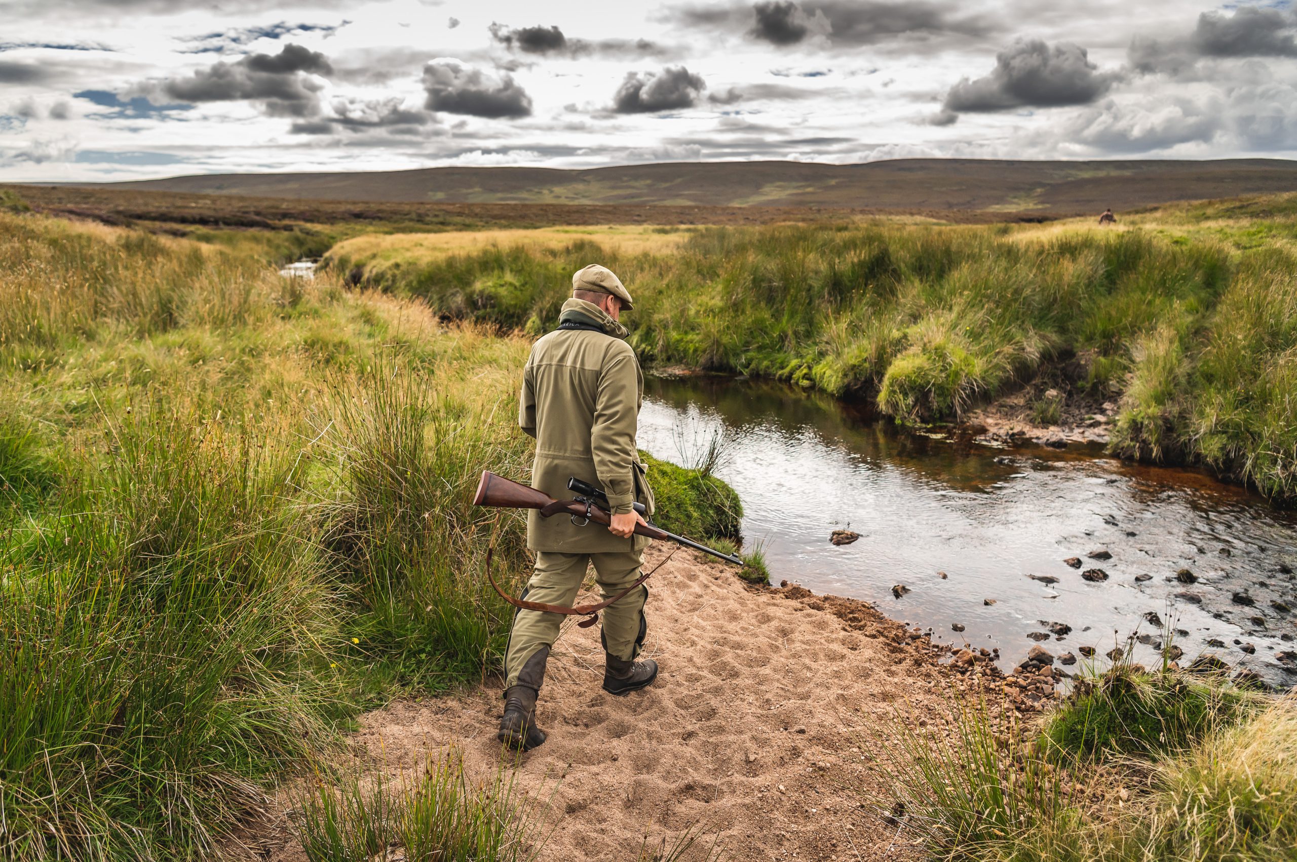 A man walking with a rifle through a river