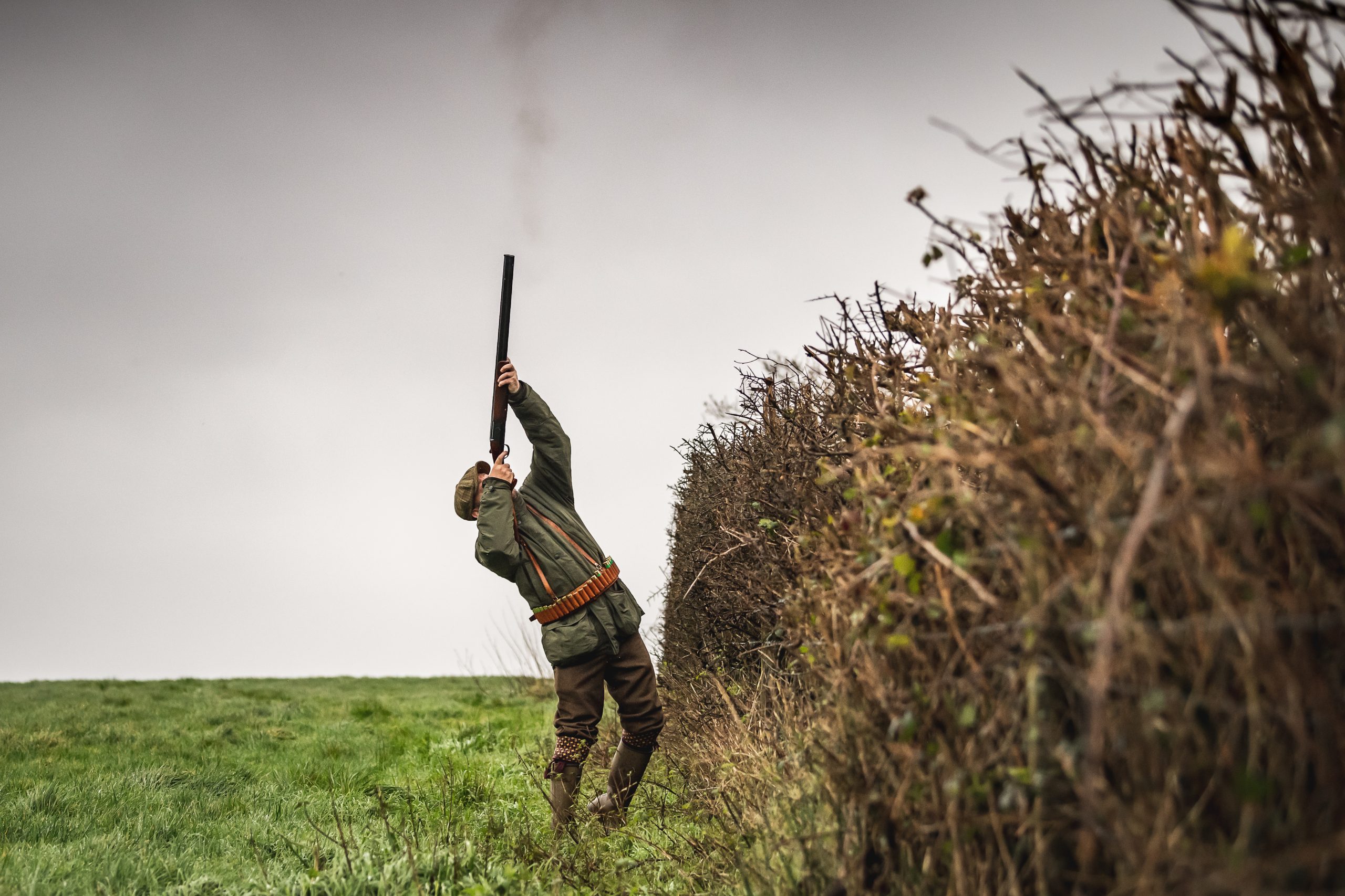 A man standing close to a hedgerow shooting