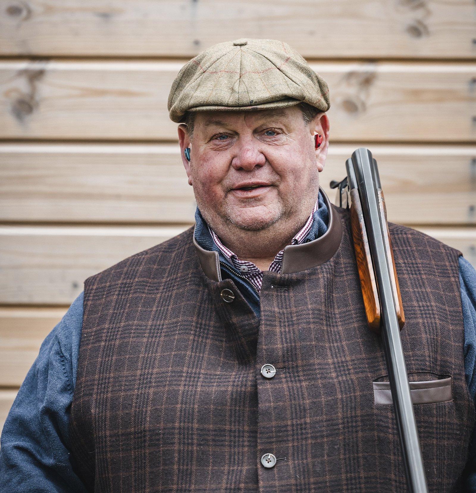 George Digweed MBE holding a shotgun, wearing a tweed waistcoat and flat cap