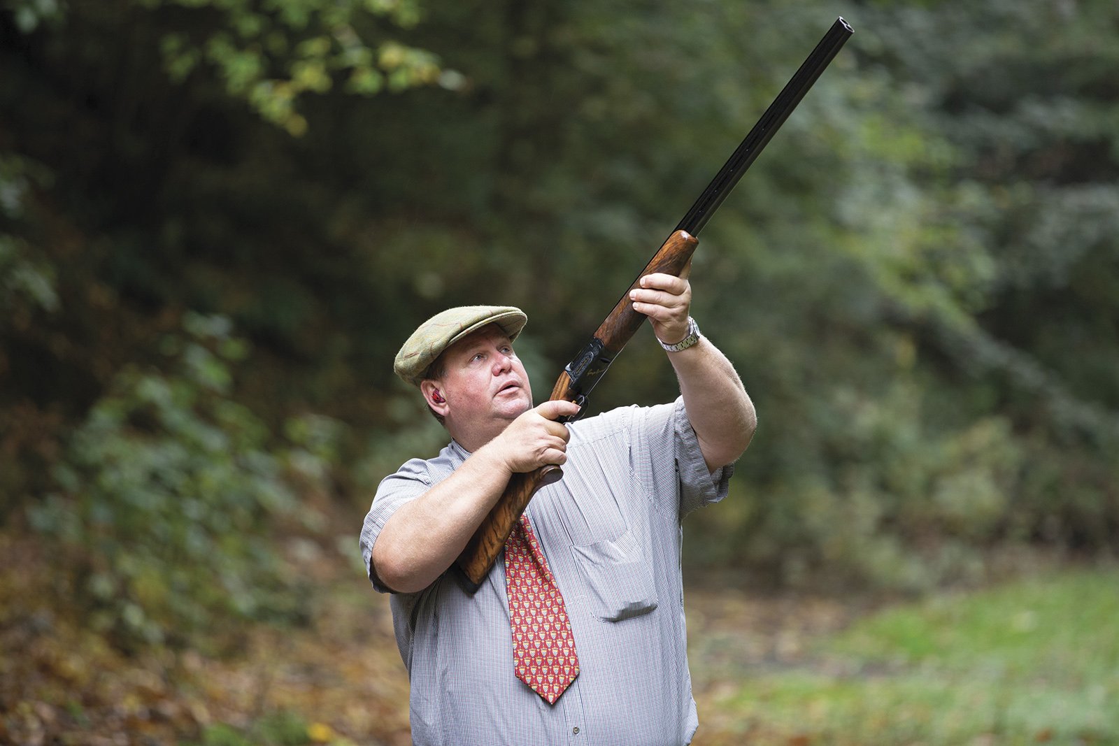 George Digweed shooting a shotgun outdoors, demonstrating his technique in woodland