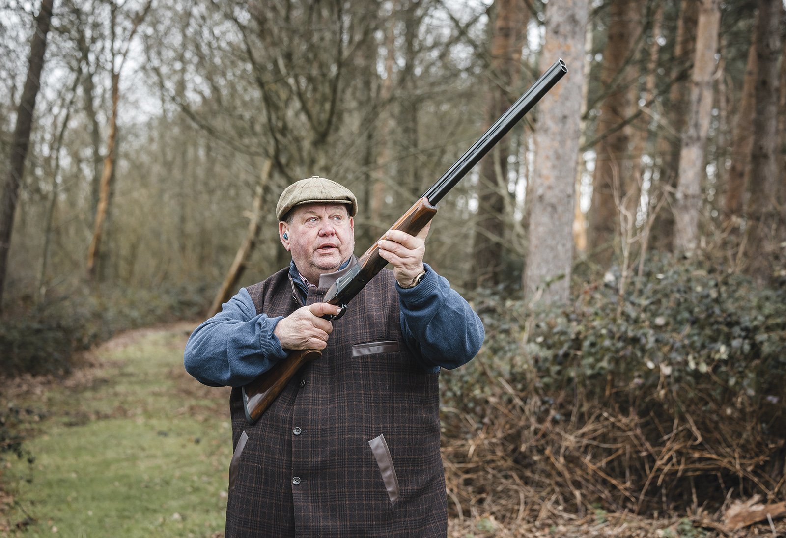 George Digweed shooting in woodland with a shotgun raised, wearing tweed