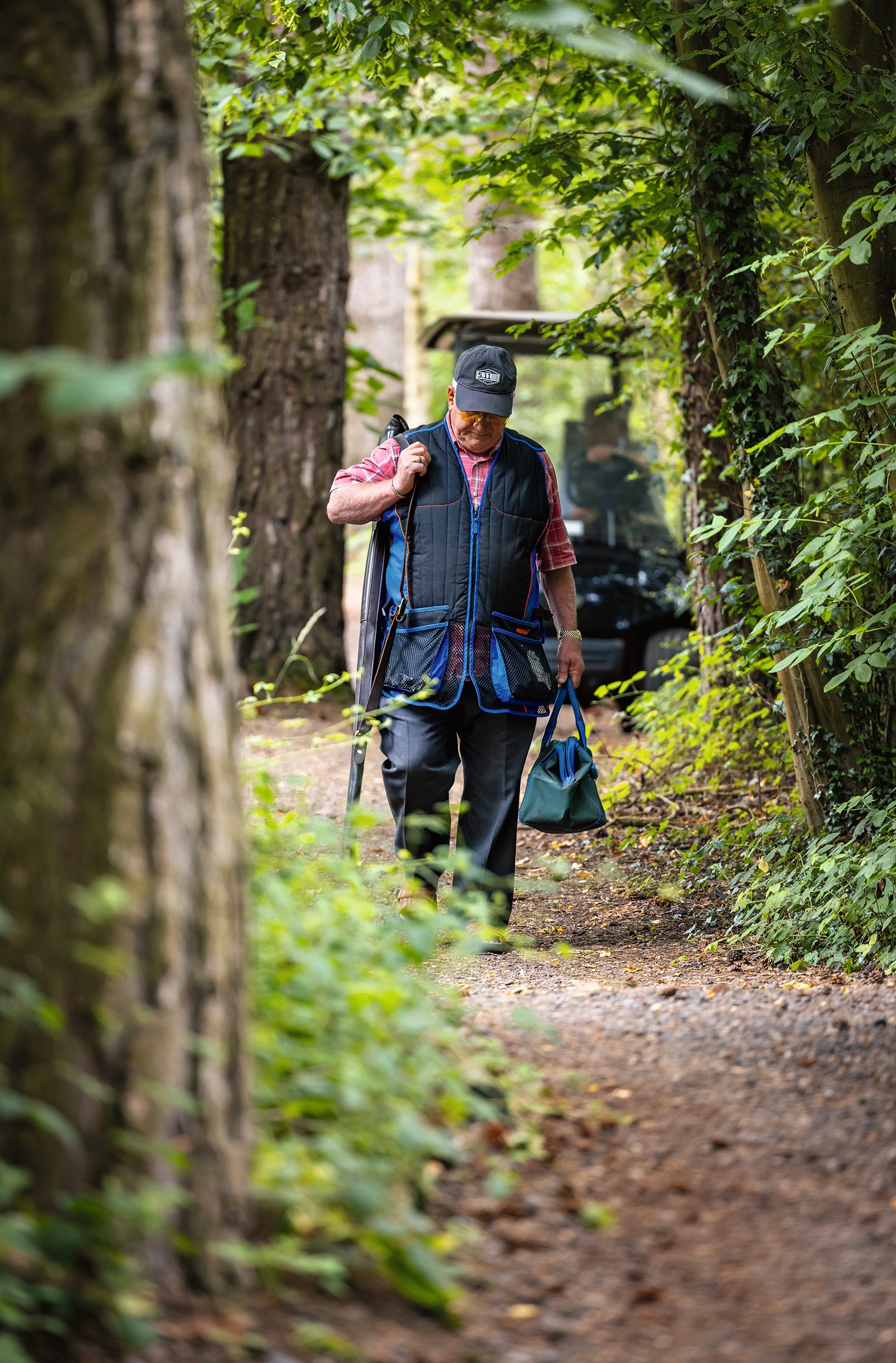 Shooter walking a wooded path with gun slip and cartridge bag at High Lodge shooting ground in Suffolk