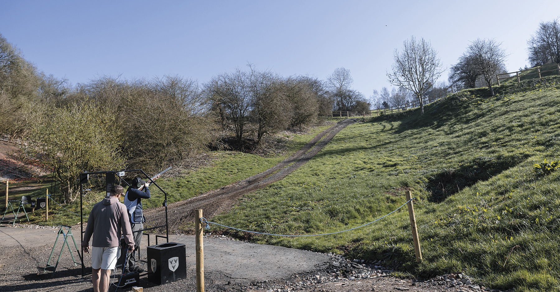 Matt Kidd shooting at a clay stand at Eaton Hall with instructor Phil Gray watching
