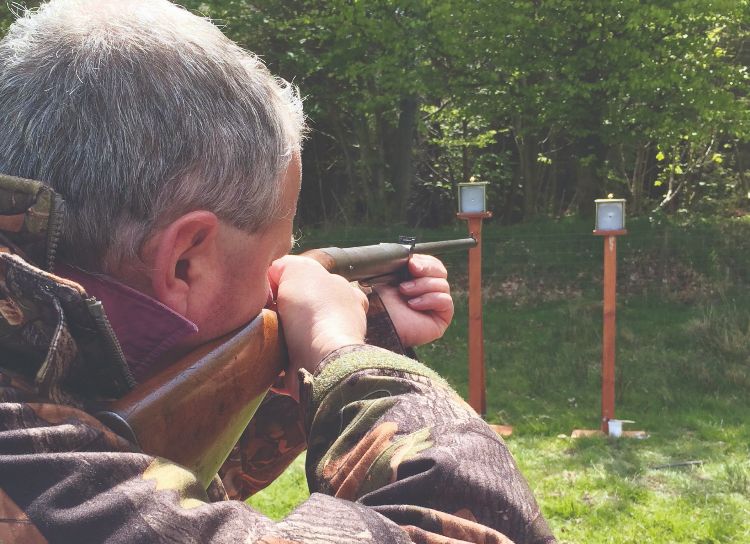 A man shooting an air rifle at a target, standing, using open sights