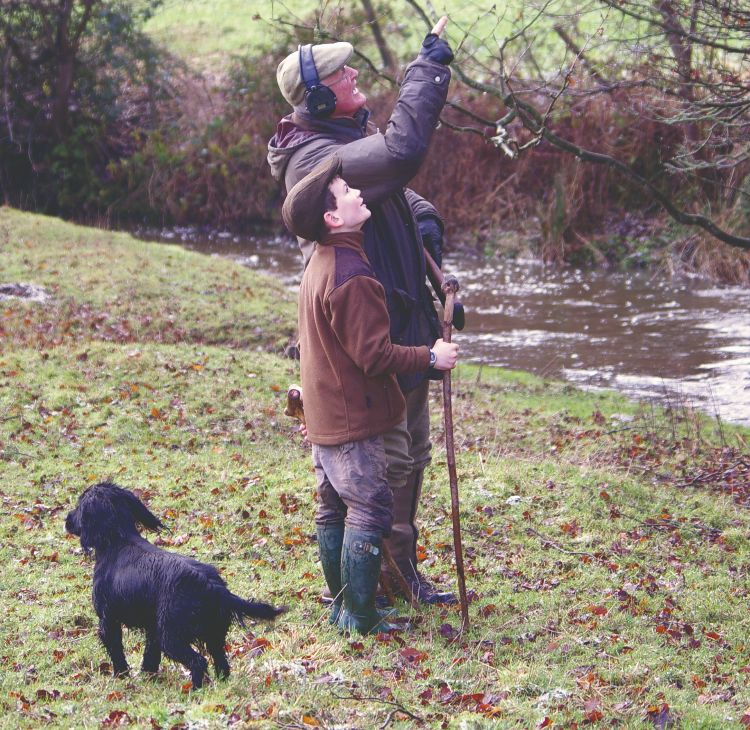 Two people shooting with a black spaniel by their feet